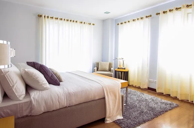 A bright bedroom with linen curtains and a soft rug