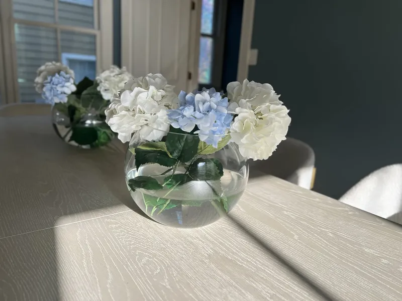 Hydrangeas in a glass globe vase on a dining table in the sun
