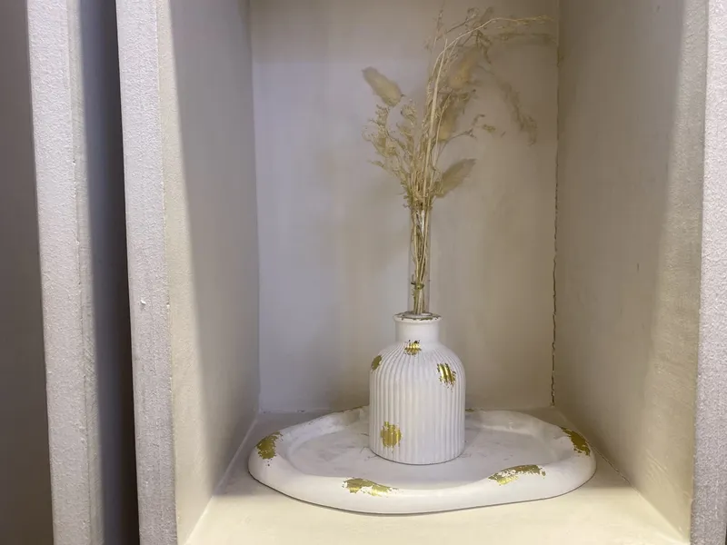 A ribbed white vase with dried grasses in a wall niche