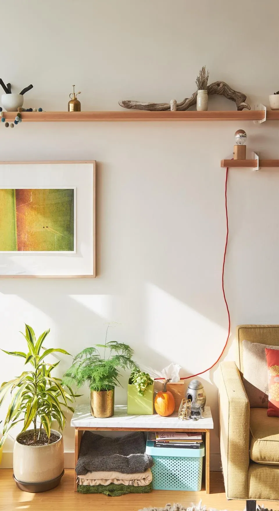 A shelf with plants, books and a framed print above a small table